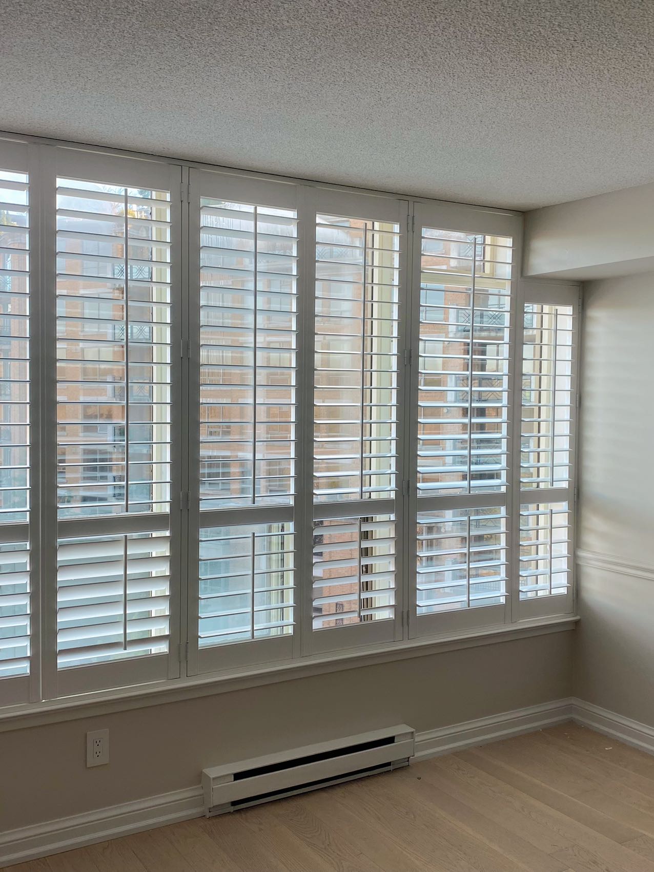 Full-height white vinyl shutters across a wide condo window